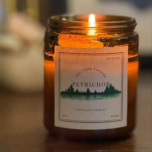 Petrichor candle lit on a wooden surface. Hand poured candles by Fair Cake Candles.