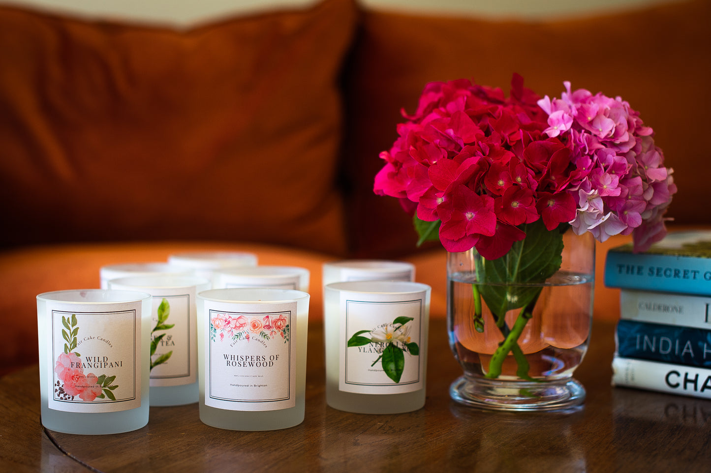 Set of candles with floral labels on a table next to a vase with pink flowers.