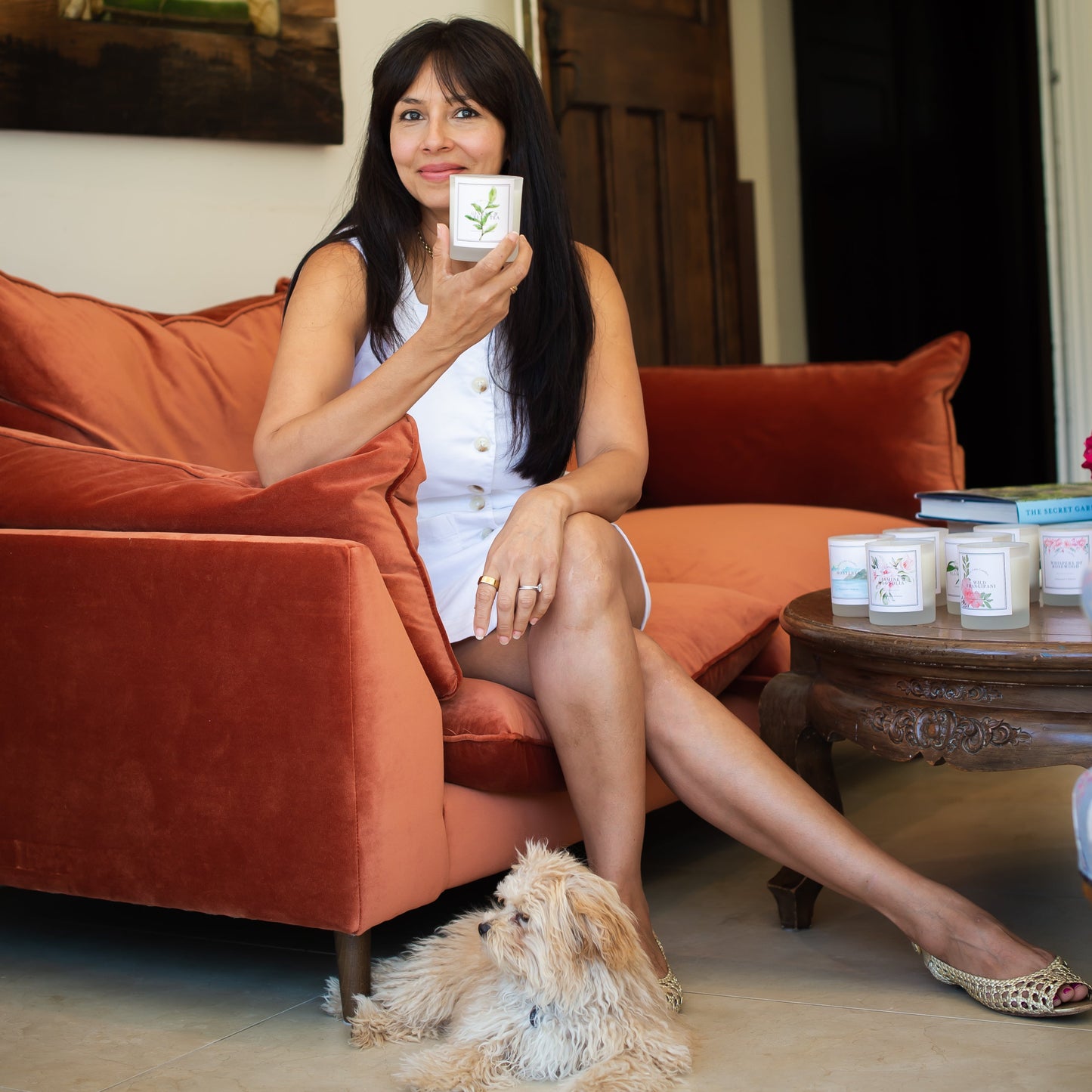 Woman sitting on an orange sofa holding a ginger and green tea candle, with a dog beside her.