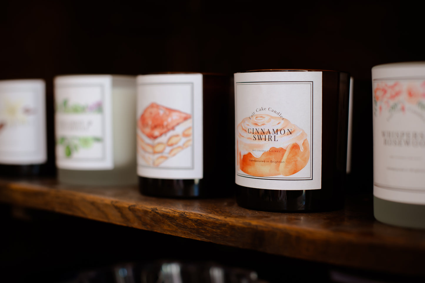Row of candles with labels on a wooden shelf against a dark background
