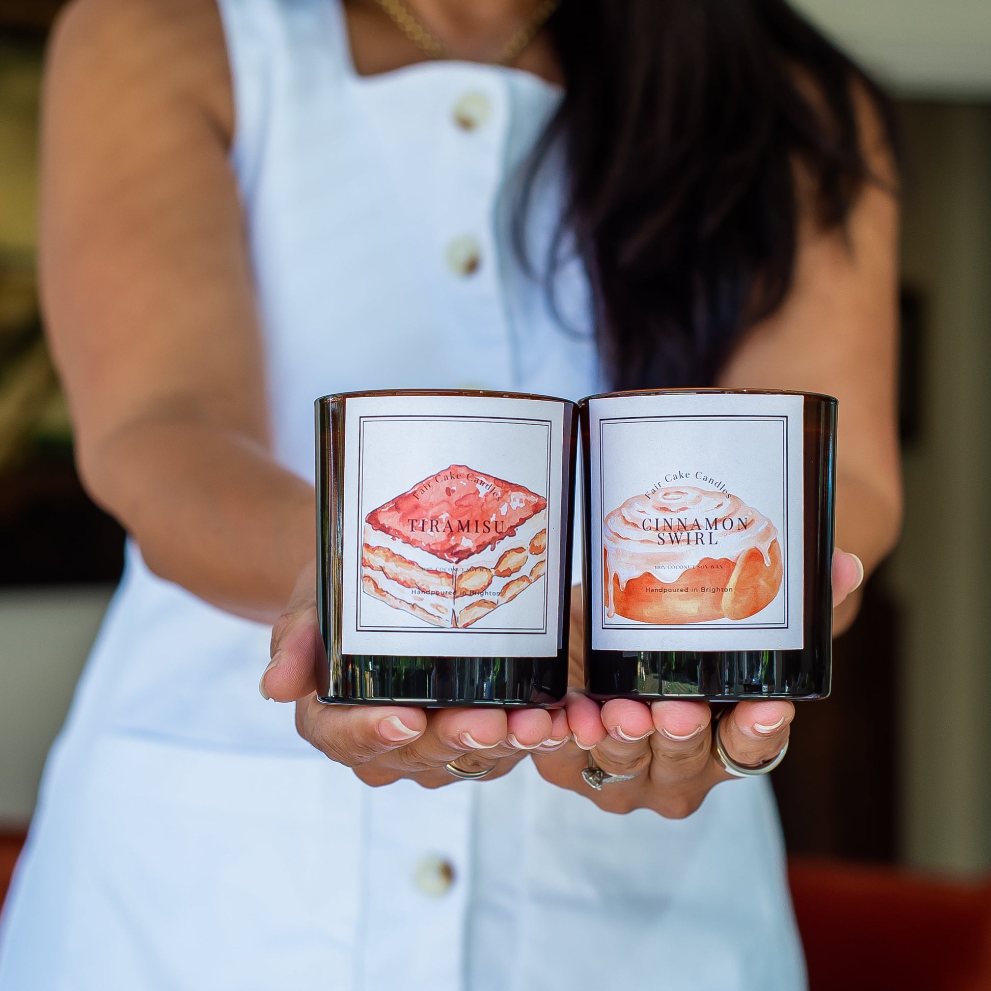 Woman holding two dessert scented candles, tiramisu scented and cinnamon swirl scented candles. Hand poured soy wax candles by Fair Cake Candles.