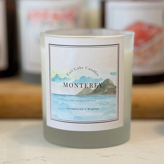 Fair Cake Candles Monterey candle with a label featuring a mountain and ocean design.
