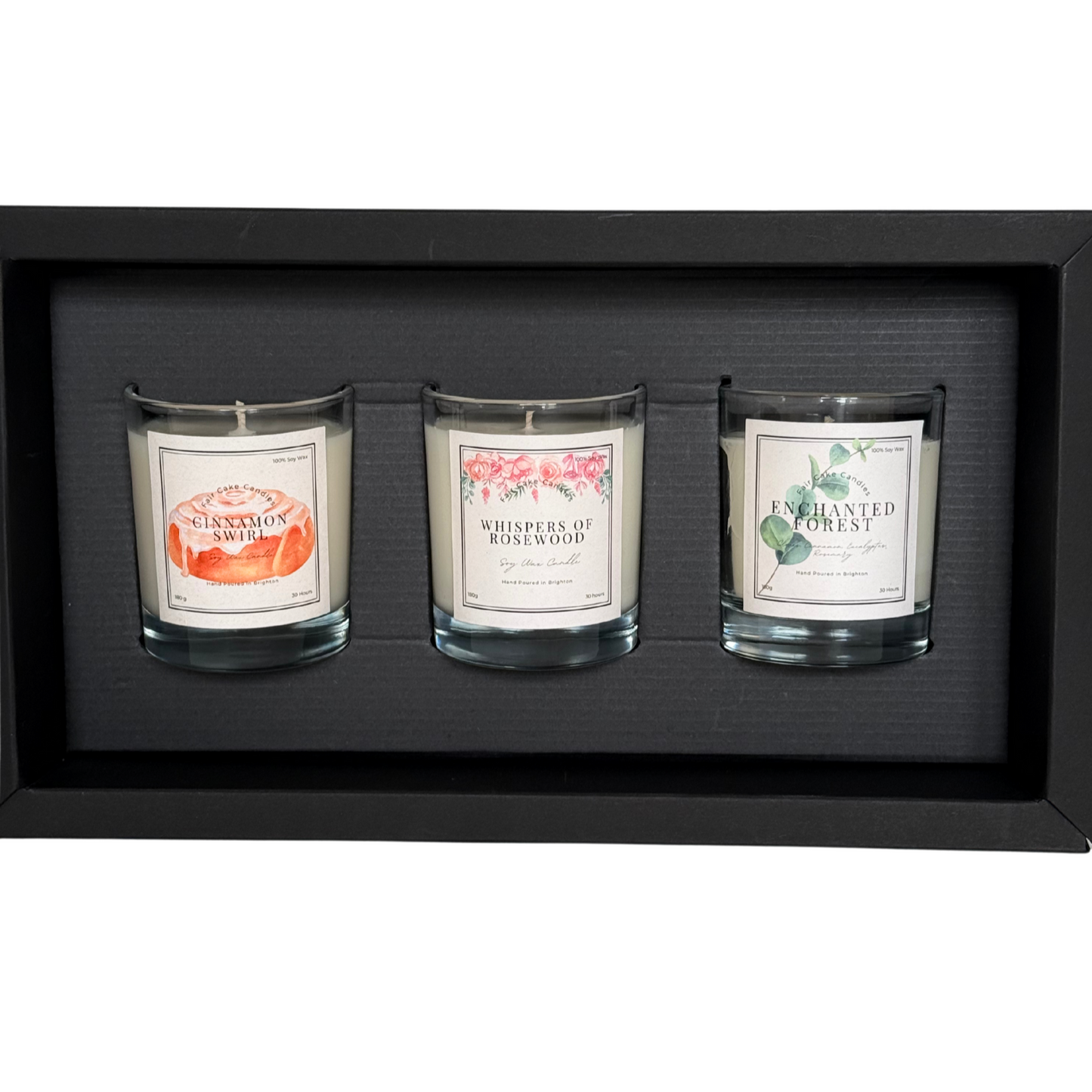 Three scented candles in glass holders with labels in a black display box.