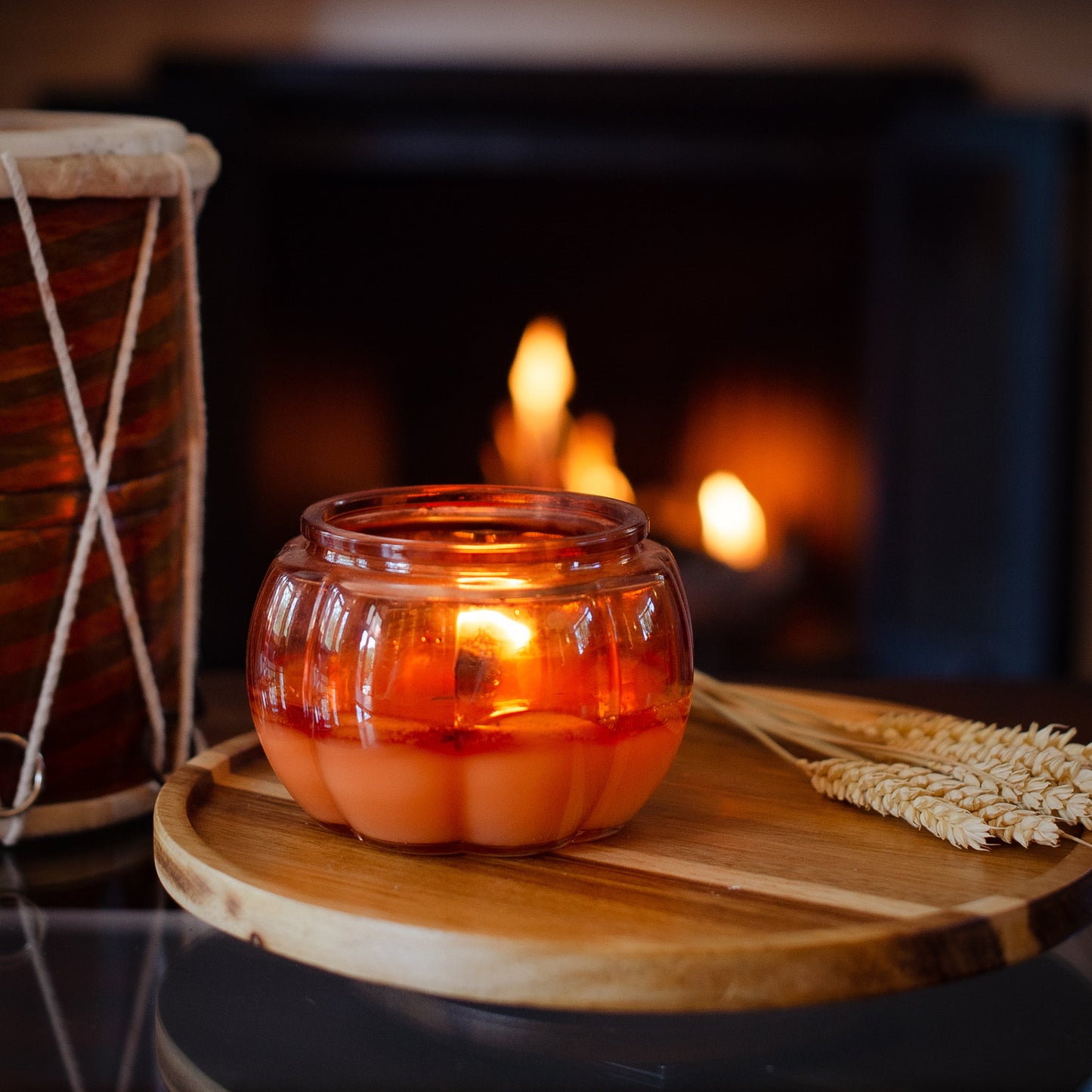 Pumpkin Candle in a glass holder on a wooden surface with a fireplace in the background
