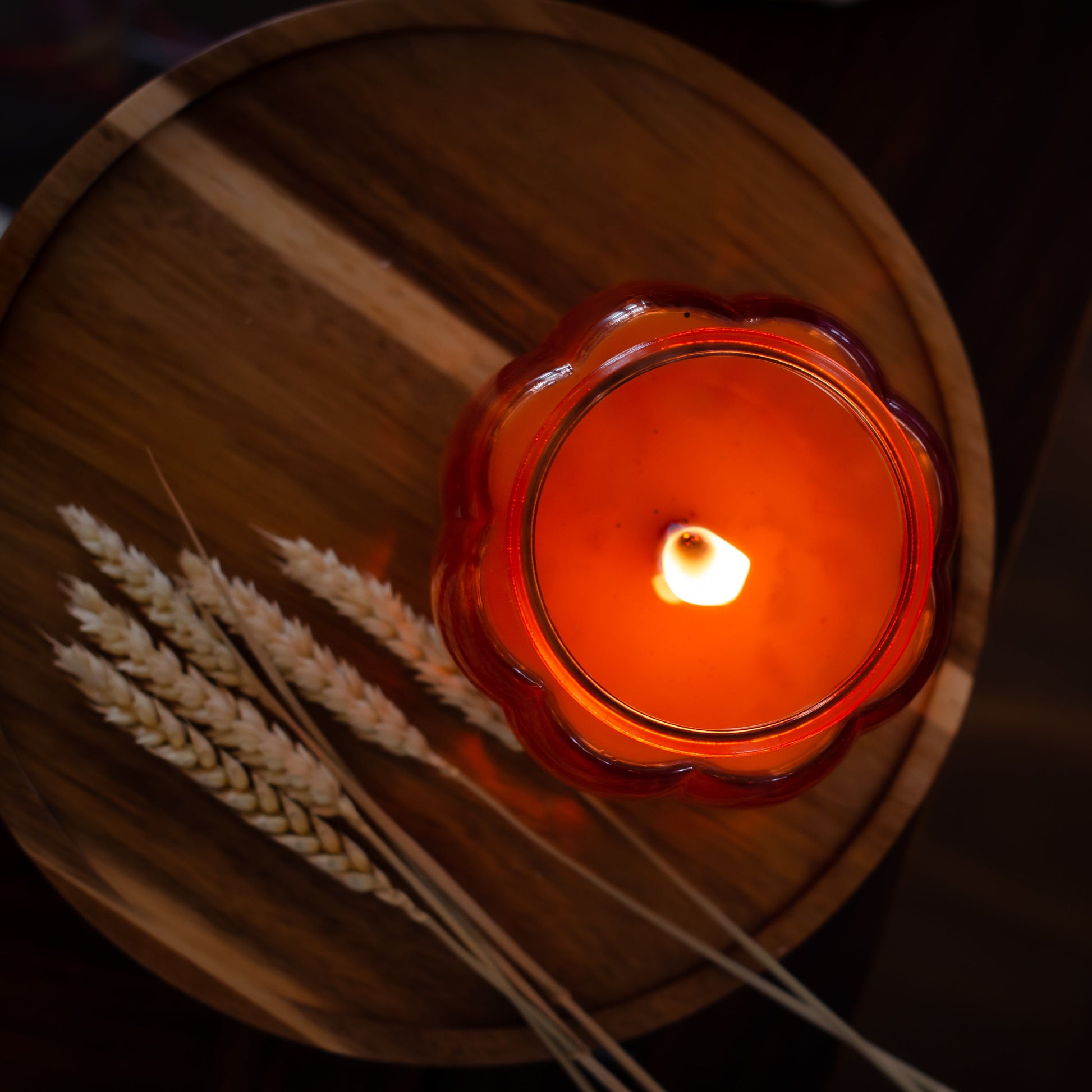 Pumpkin Candle in a glass holder on a wooden surface with wheat stalks.